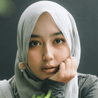 woman wearing gray long-sleeved top and gray hijab right hand on cheek