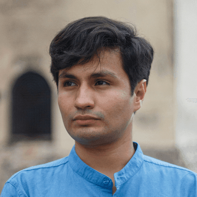 A man in a blue collared shirt stands outdoors.