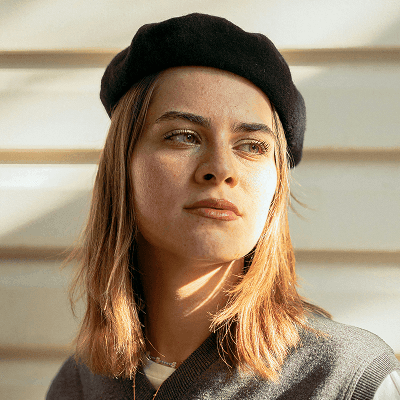 a woman wearing a black hat standing in front of a white wall
